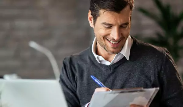 Young professional working on a computer and writing something on a notepad